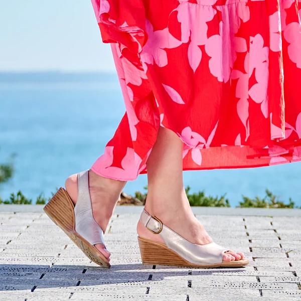 Woman standing on stone walkway wearing a red dress featuring the the Gabriella heel in metallic. Shop Dress wedges, Wedges, Wedge sandals.